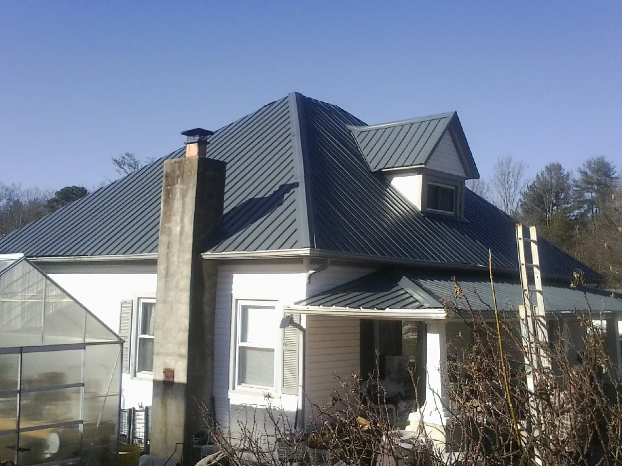 Dark blue standing seam metal roof on a white farmhouse with dormer — Slate & Tile Roof Repair by Roofing Brothers in Edelstein