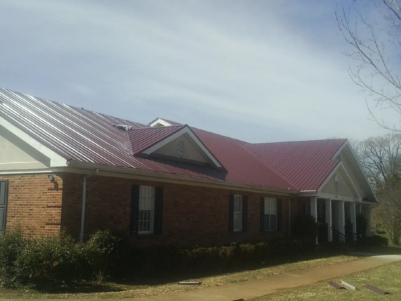 Red metal roof with gabled entries on a long brick building, from a Hail Damage Roof Repair job in Edelstein