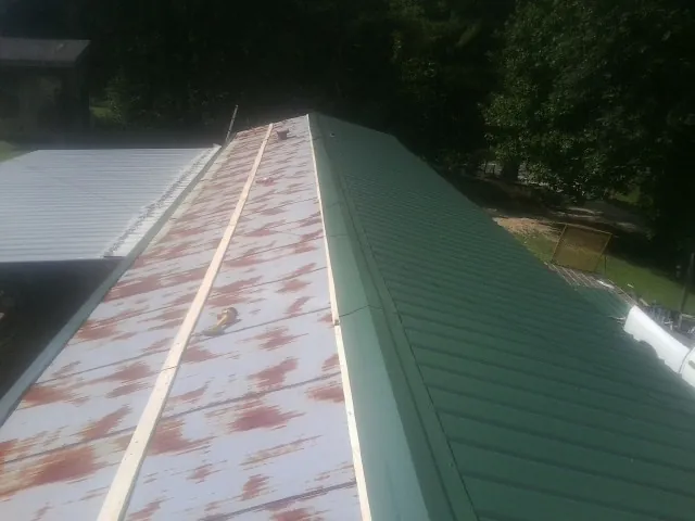 Old rusted panels beside newly installed green metal roofing — Wind Damage Roof Repair by Roofing Brothers in Edelstein
