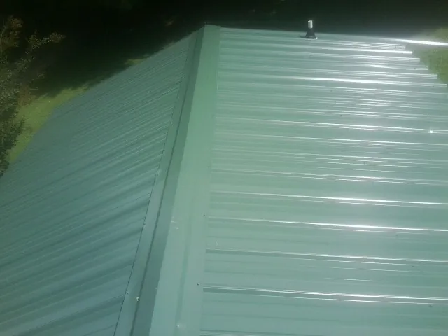 New green metal panels meeting at the ridge of a roof — Flat Roof Repair work by our crew in Edelstein