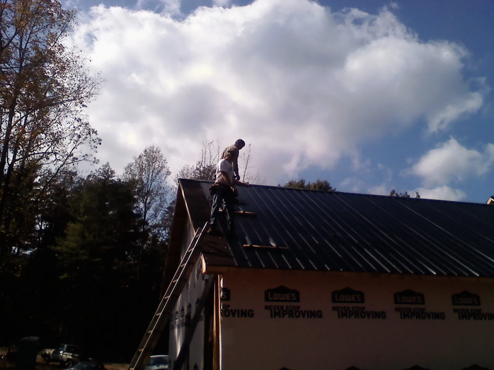 Roofer fastening dark metal panels high against a cloudy sky, from a Roof Inspection job in Edelstein