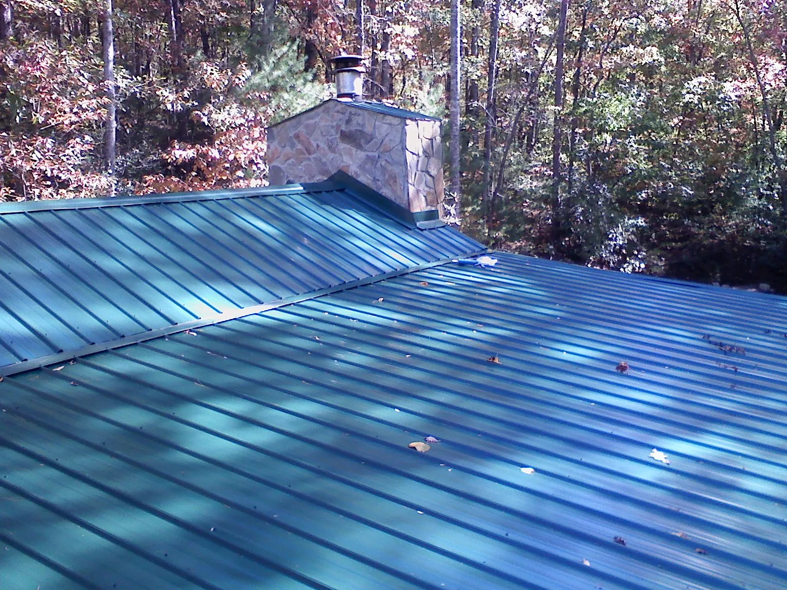 New green metal roof and stone chimney surrounded by autumn woods in Edelstein